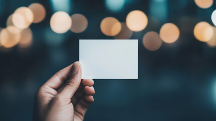 A hand holds a blank business card in front of a bokeh background.