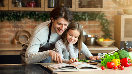 Happy dad and little daughter checking recipe in cookbook at kitchen together while cooking healthy lunch at home, free space