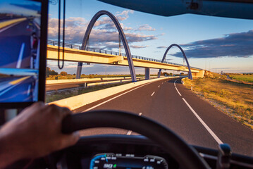 View from the driver's seat of a truck on a highway crossing under an arched bridge.