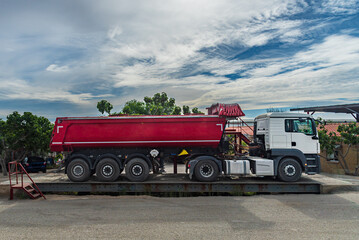 Truck with a dump semi-trailer for earthmoving mounted on an industrial weighing scale.