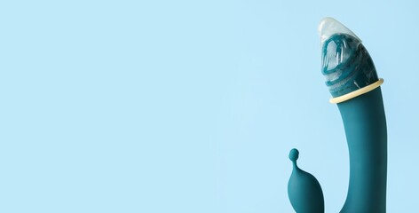 Vibrator with condom on light blue background with space for text