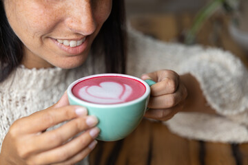 Close-up happy young woman smiling in a cafe holding a cup of matcha tea with raspberry,...