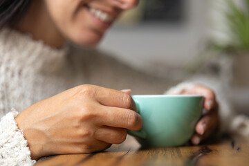Close-up happy young woman smiling in a cafe holding a cup of matcha tea, art with heart shape milk, cappuccino coffee with foam and heart, espresso coffee, decoration with plants, vegan hot drink
