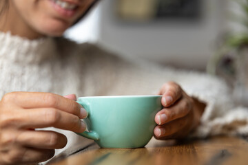 Close-up happy young woman smiling in a cafe holding a cup of matcha tea, art with heart shape milk, cappuccino coffee with foam and heart, espresso coffee, decoration with plants, vegan hot drink
