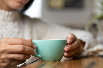 Close-up happy young woman smiling in a cafe holding a cup of matcha tea, art with heart shape milk, cappuccino coffee with foam and heart, espresso coffee, decoration with plants, vegan hot drink
