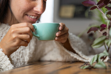 Close-up happy young woman smiling in a cafe holding a cup of matcha tea, art with heart shape milk, cappuccino coffee with foam and heart, espresso coffee, decoration with plants, vegan hot drink
