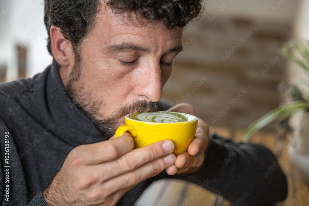 Wall mural close-up happy young man smiling in a cafe holding a cup of matcha tea with raspberry, heart-shaped 