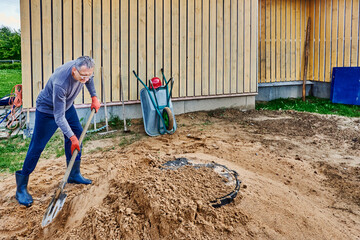 Construction worker compacts sand around septic tank lid using bayonet shovel.