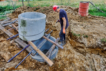 Installation of septic tank made of concrete rings for suburban sewerage system, worker pushes rings one over other.