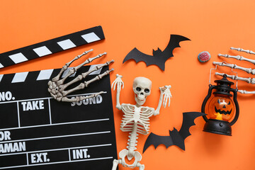 Clapperboard with different Halloween decor on orange background