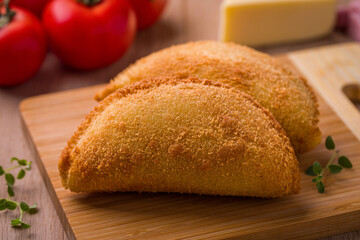 Delicious Crispy Empanadas on a Wooden Cutting Board with Tomatoes