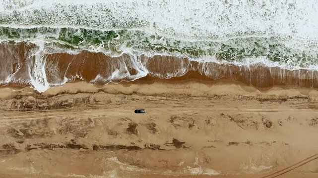 Car on beach at foreshore between Atlantic waves and dunes of Naukluft desert, Walvis Bay, Namibia