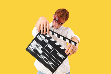 Young man dressed for Halloween as zombie with movie clapper on yellow background