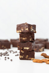 Close Up of Chocolate Pecan Fudge on a White Background with Chocolate Pieces and Pecans Scattered Around