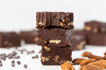 Close Up of Chocolate Pecan Fudge on a White Background with Chocolate Pieces and Pecans Scattered Around; Bite Taken out of One  Piece
