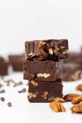 Close Up of Chocolate Pecan Fudge on a White Background with Chocolate Pieces and Pecans Scattered Around; Bite taken out of One Piece