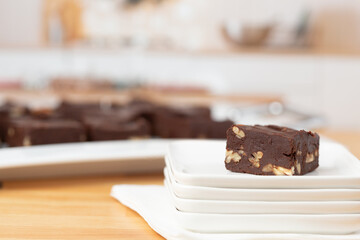 Piece of Homemade Chocolate Pecan Fudge on a White Plate with Tray of Fudge in Background in a Kitchen Decorated for Christmas