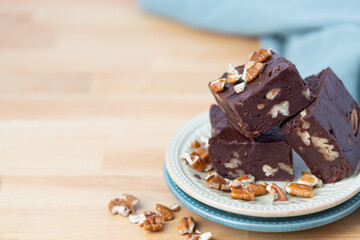 Three Pieces of Homemade Chocolate Pecan Fudge on a Plate with Pecan Pieces Scattered Around on a Kitchen Countertop