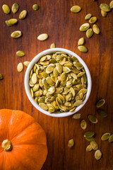 Bowl of Fresh Pumpkin Seeds on Wooden Table with Pumpkin