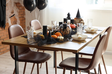 Festive table setting with pumpkins and burning candles for Halloween party in light room