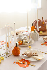 Festive table setting with pumpkins, burning candles and golden cutlery for Halloween party at home