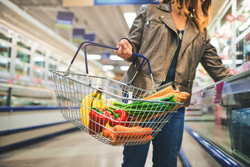 Woman, basket and hands for browsing in supermarket, goods discount and shelves for deal. Female...