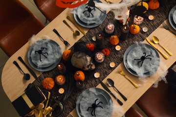 Festive table setting for Halloween party with burning candles, pumpkins, spiders and web