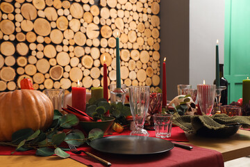 Festive table setting with Halloween pumpkins, burning candles and leaves in dining room