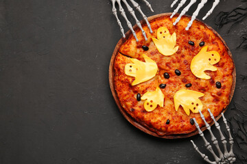 Wooden board with tasty pizza and decorations for Halloween party on black background
