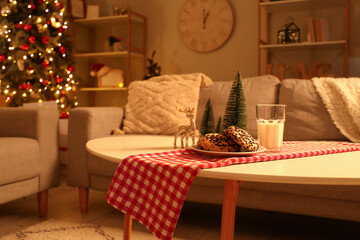 Christmas cookies with glass of milk and decor on table in living room at night