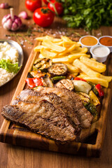 Delicious Grilled Steak with French Fries and Vegetables on Wooden Board