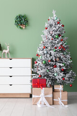 Decorated Christmas tree with gifts and dresser against green wall
