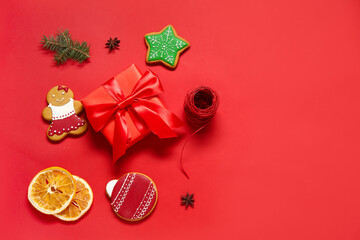 Tasty Christmas cookies with gift box and decor on red background