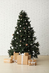 Beautiful Christmas tree with gift boxes near white brick wall