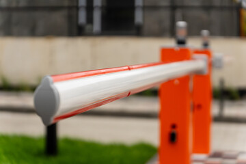 The barrier arm stretches across the entrance, poised to control vehicle access. Bright orange and silver colors catch the sunlight as vehicles approach