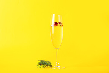 Glass of champagne with Christmas balls and fir branch on yellow background