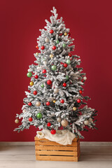 Fir tree decorated with different Christmas balls near color wall