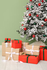 Beautiful decorated Christmas tree with gifts near green wall