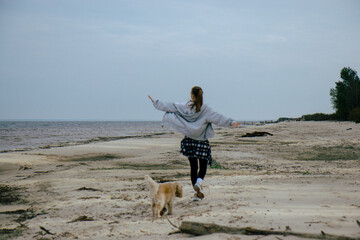 Carefree young woman walking along the coast, arms open wide, symbolizing a sense of freedom and connection with nature. A peaceful moment on a quiet autumn beach. With her dog, Cocker Spaniel