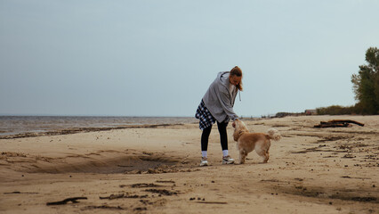 Young woman enjoying a game of fetch with her dog by the sea. The dog runs after a ball, while the girl smiles, reflecting joy and companionship in a beachside environment.