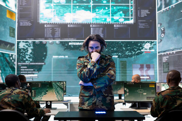 Young army conscript checking mission data and details on a hologram projection, studying operation briefings in military command center. Soldier looks at CCTV radar imagery on 3d visualization.