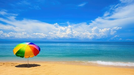 A vibrant beach umbrella rests on the sandy shoreline overlooking a calm ocean beneath a clear blue sky
