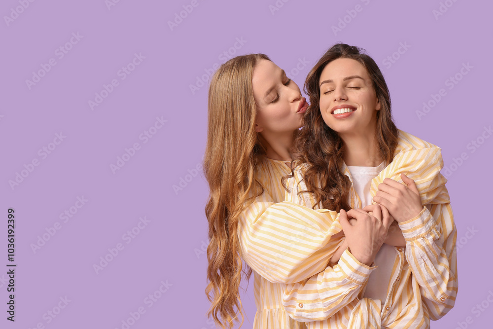 Wall mural Beautiful young woman hugging her sister on lilac background