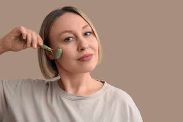 Woman using face massage roller on beige background