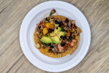 Overhead view of delicious looking tostada exotica stacked high on a tortilla and topped with chopped fruit and avocado for an excellent Mexcian seafood meal