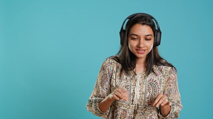 Indian woman playing music, having fun moving on rhythm, pretending to use turntables. Upbeat DJ wearing headphones, producing beats, isolated over studio background, camera A