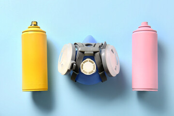 Respirator and spray paint cans on blue background