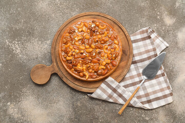 Wooden board of sweet tart with different nuts and caramel on grey background