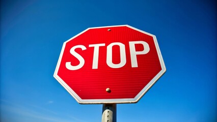 Obraz premium Red stop sign is standing against a blue sky, with white clouds passing by