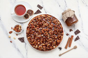 Sweet tart with different nuts and cup of tea on white background
